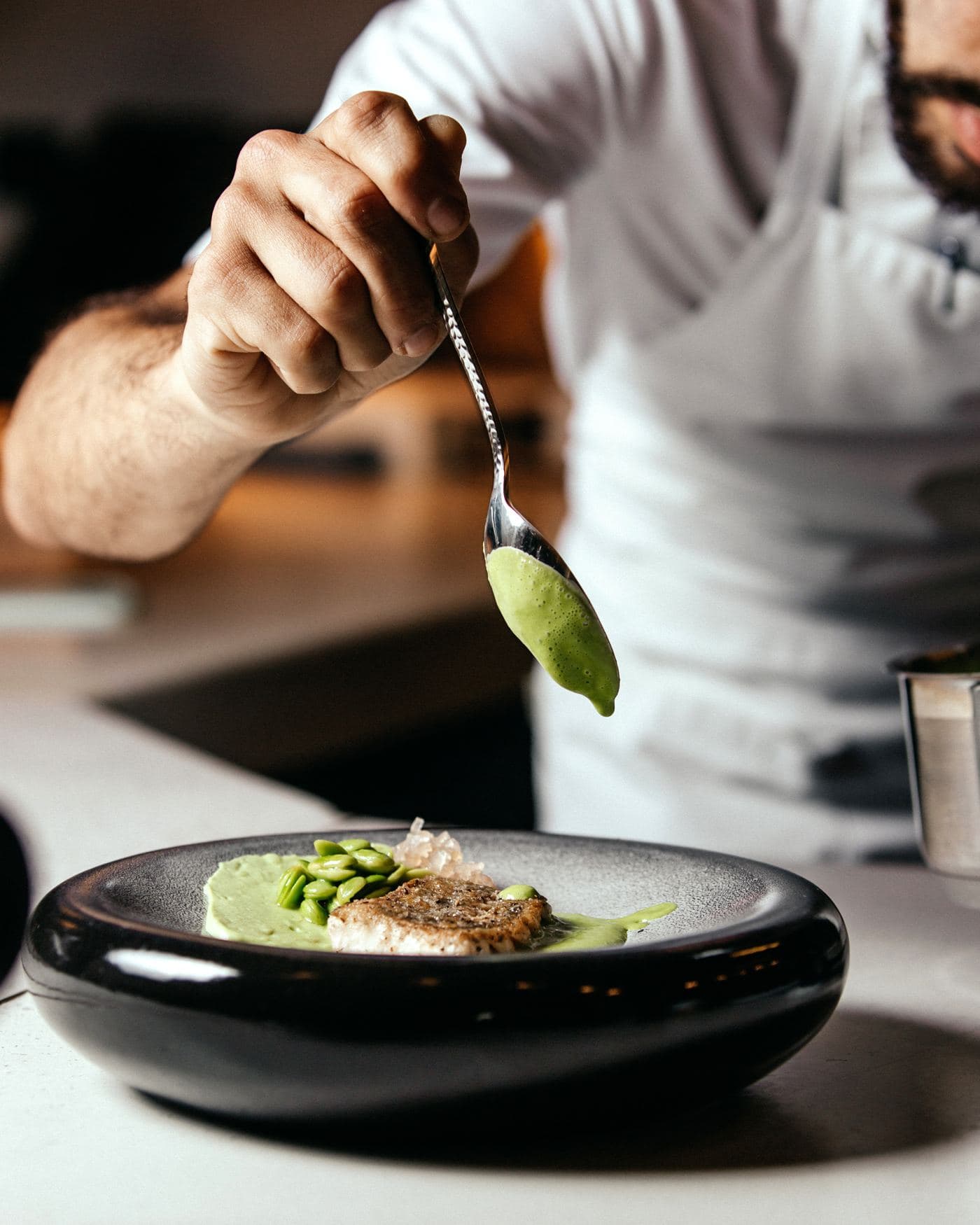 Ein Koch richtet ein Fischgericht mit grüner Sauce an
